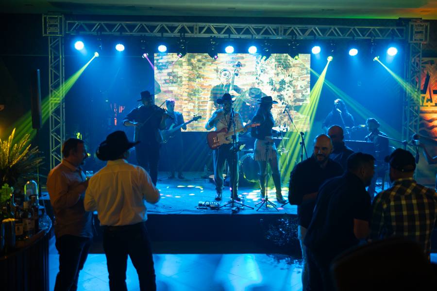 Convidados dançando em frente ao palco com telão e luzes
