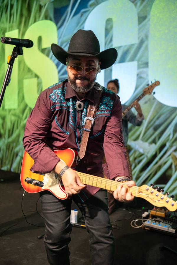 Vocalista de chapéu com guitarra diante do telão da Stoller
