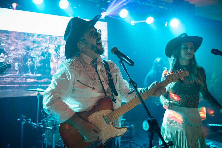 Vocalistas de chapéu no palco com telão